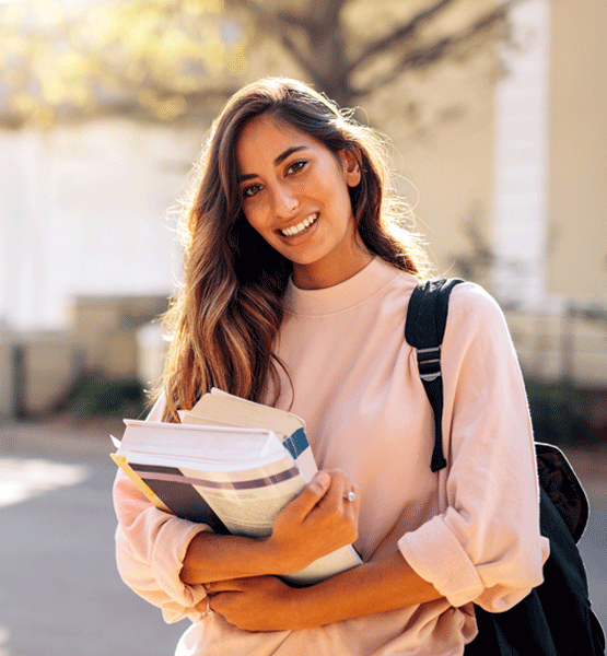 College student outside of a college holding textbooks.