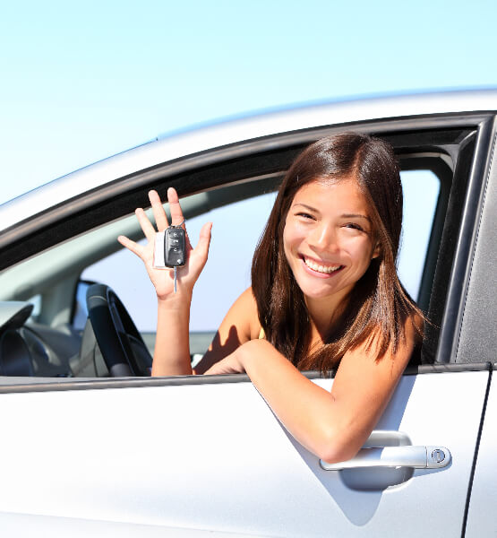 Young women holding her car keys sitting in the driver side of her new silver car. 