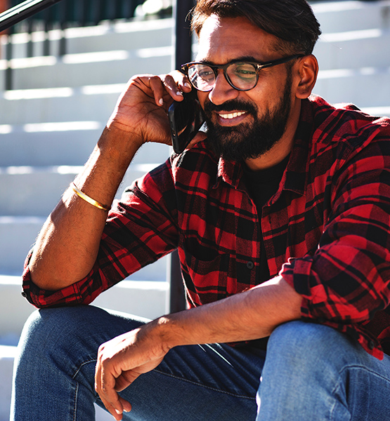 Middle aged man with glasses and beard sitting on stairway outdoors smiling and talking on cellphone