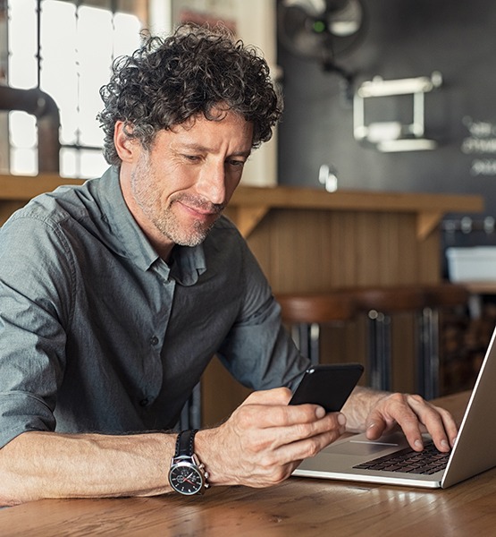 Middle aged bar owner looks up information on his laptop and dials a phone number on his cellphone