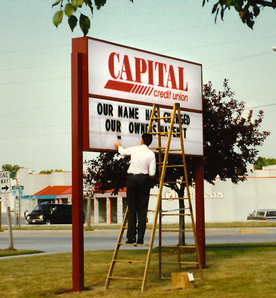 Photo from the 90's showing a staff member climbing a ladder to manually add messaging to a marquee