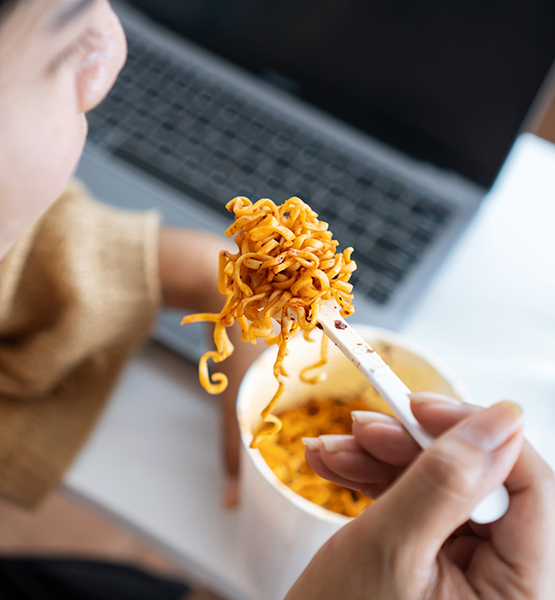 Person eating cup ramen at desk in front of laptop