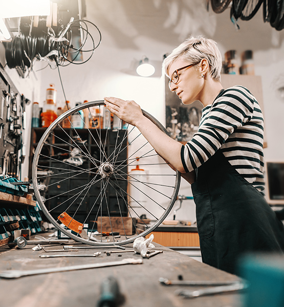 Female bike repair shop staff looks over bike components at work table surrounded by repair tools