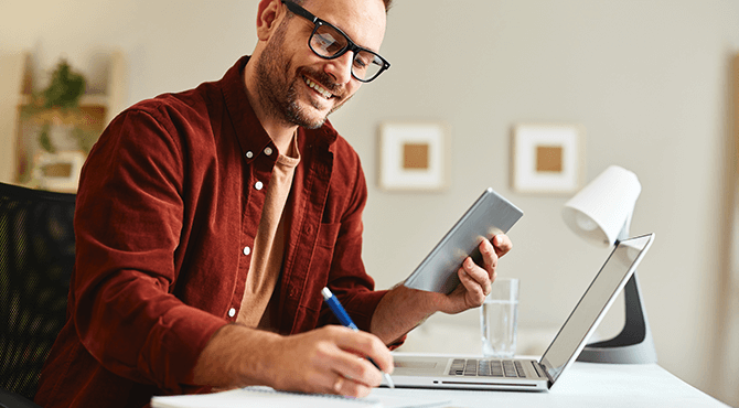 man smiling and writing, looking at the screen.