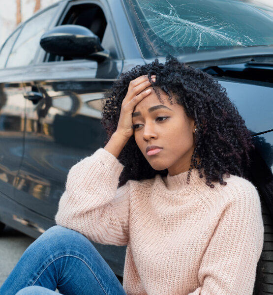 Lady sitting by her wrecked car with her hand on her head.