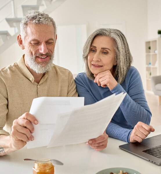 Middle aged man and woman looking at account comparisons on paper and laptop.