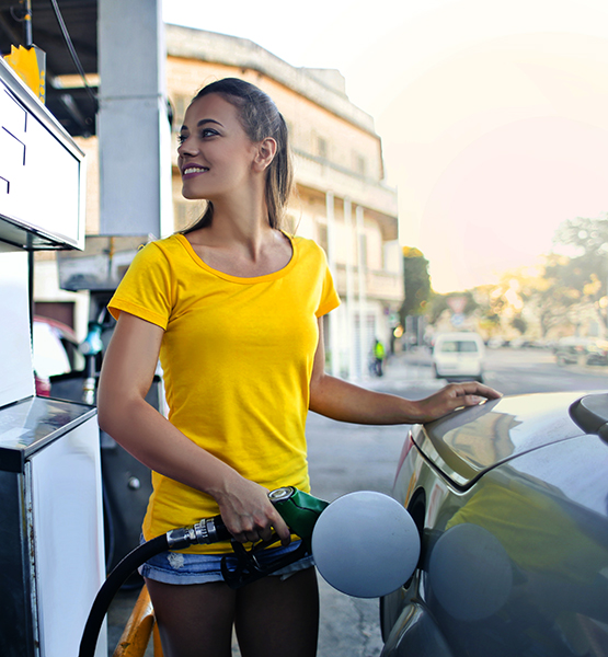 Young smiling woman fueling her car at the gas pump