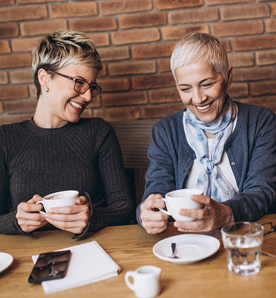 Middle aged woman and elderly friend sit at a restaurant table while laughing over coffee together