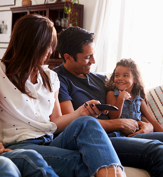 A family of a father mother and daughter enjoying TV together on couch in living room of their home