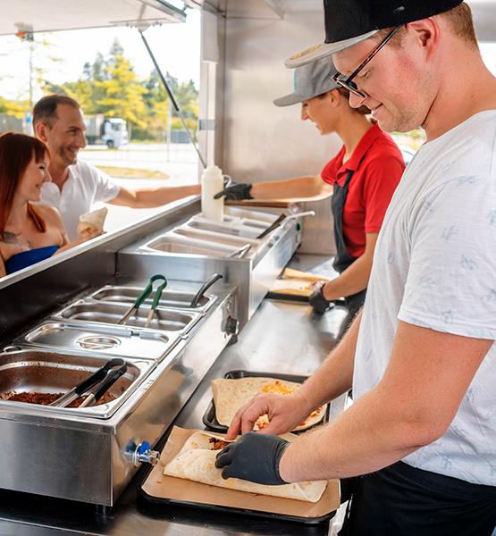 Workers inside a taco food truck prepare burrito order for customers waiting outside the truck