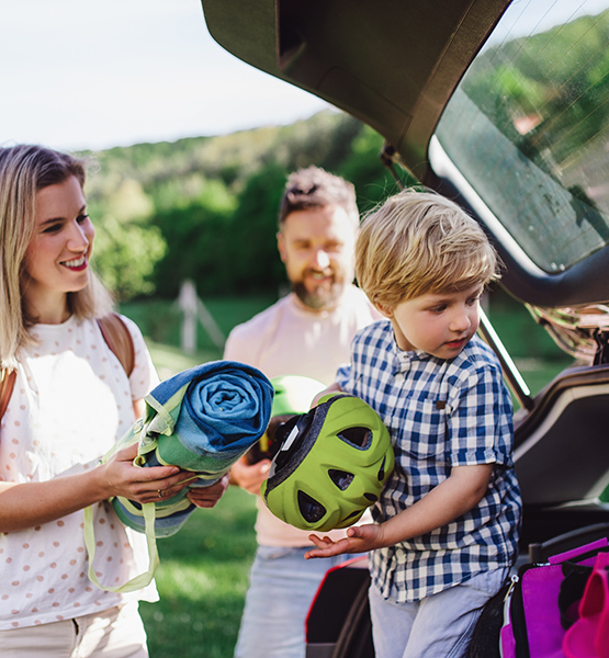 Mother father and toddler smile while unloading biking gear from family vehicle on vacation trip