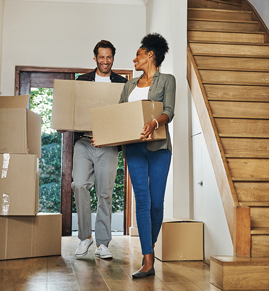 Middle aged man and woman carry boxes into entryway of newly purchased house