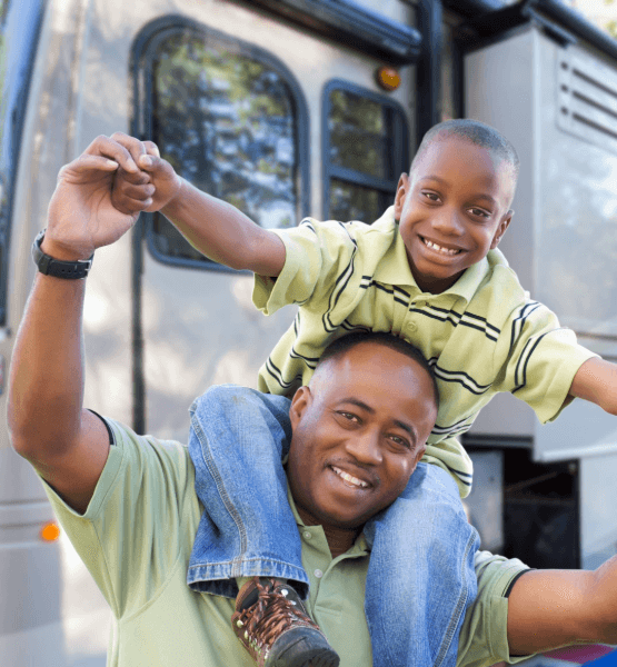 Happy father with son sitting on his neck standing outside of new RV.