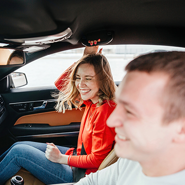 Young man driving a sedan with female friend laughing, found the perfect car 
with Capital Carfinder.