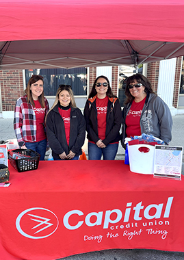 Staff pose in Capital Credit Union branded t-shirts under a sponsorship tent at local farmers market