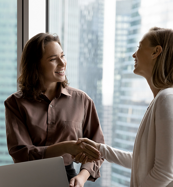 Two middle aged women shaking hands and chatting with a smile