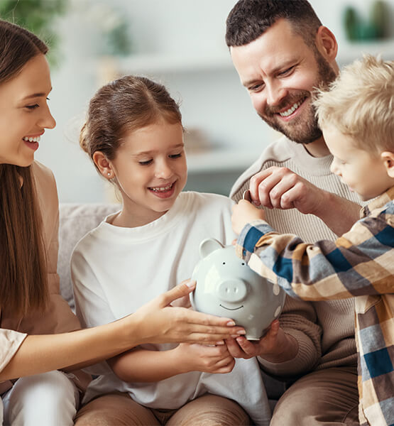 Parents holding piggy bank and kids putting coins inside.
