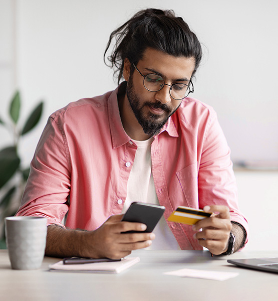 man in a red shirt looking at phone and credit card