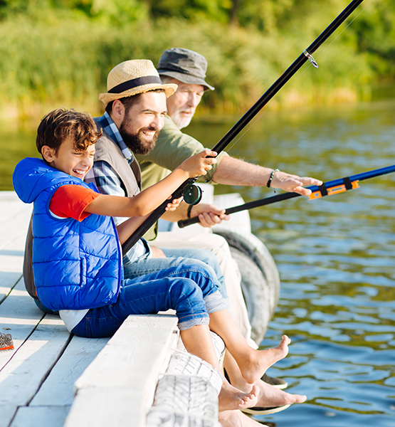 Grandfather father and son sitting on a dock over a lake and having fun fishing together