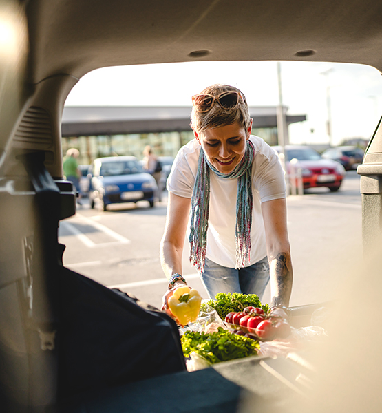 Happy mature woman running errands unloads fresh produce and  groceries into SUV vehicle