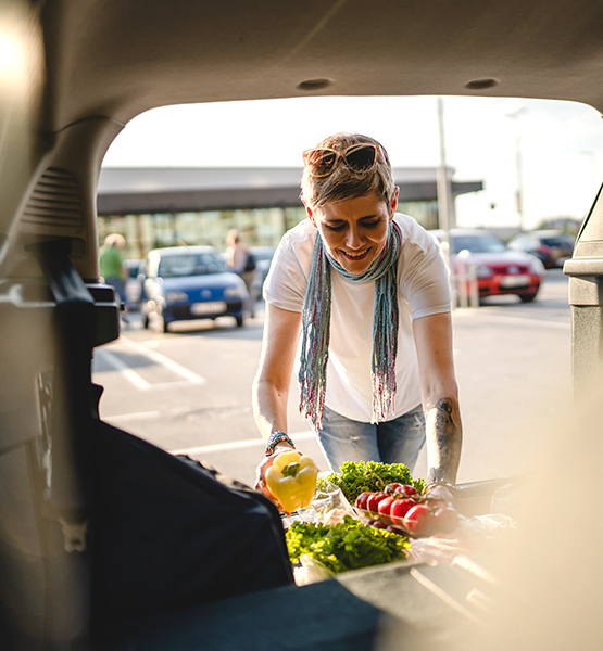 Happy mature woman running errands unloads fresh produce and groceries into SUV vehicle