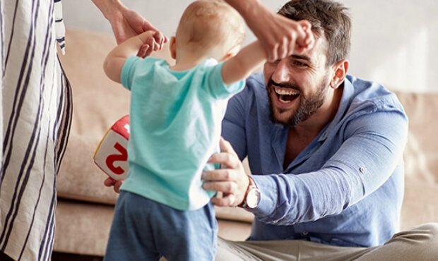 Couple inside of home, young lady walking toddler with man holding him.