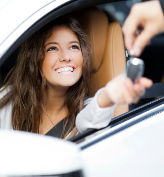 Woman smiling in drivers seat of her car taking the keys
