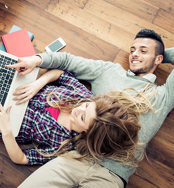 Young man and woman laying on floor together while browsing the internet on laptop
