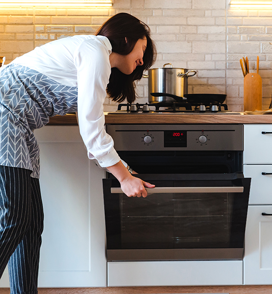 Middle aged woman opening oven door in her kitchen to check on what she's baking