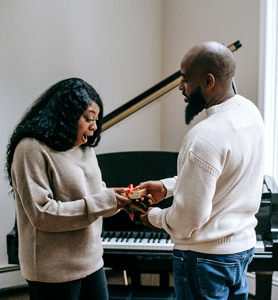 Middle aged man giving wife a small box wrapped in red ribbon containing an expensive holiday gift