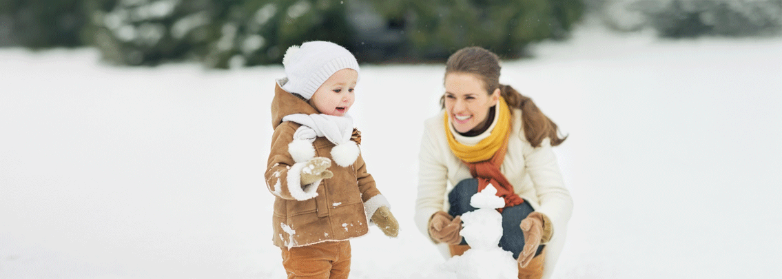 Mom and toddler making snowman outside. 