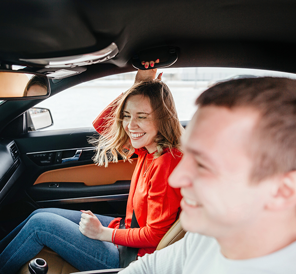 Young man driving a sedan with female friend laughing, found the perfect car 
with Capital Carfinder.