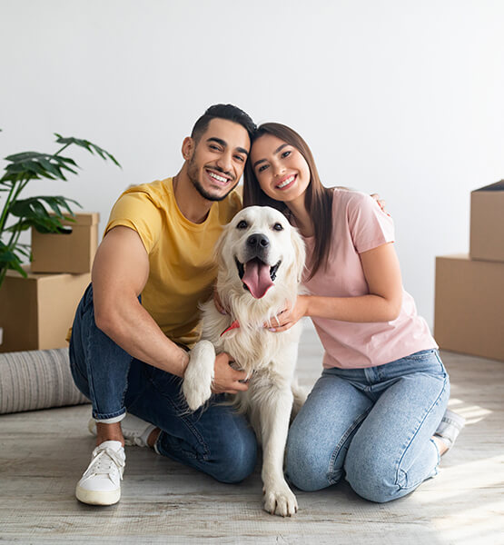 Happy couple and golden retriever inside of a new home with boxes surrounding them.