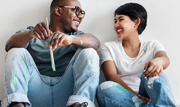 Couple in tshirt and jeans with paint stains in home.