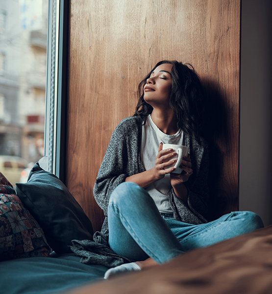 Young woman peacefully relaxing at home and breathing deeply with a mug of soothing tea