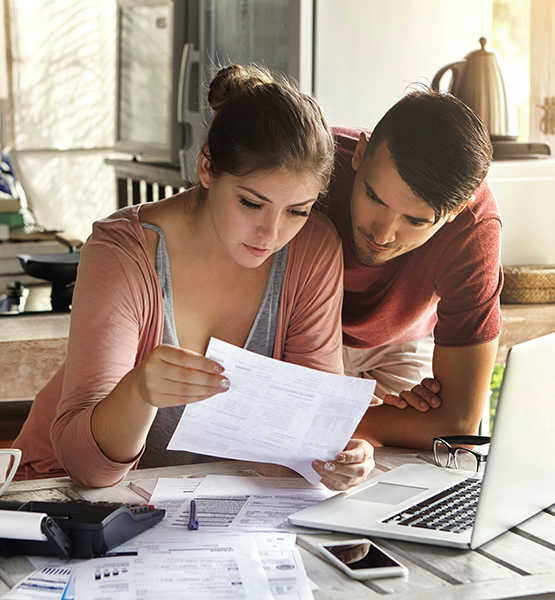 Young adult man and woman examining financial documents at desk in front of laptop and cellphone