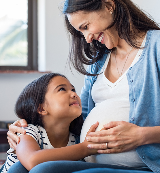 Pregnant mother smiles as young daughter rests her hand on mom's pregnant belly to feel baby kicks