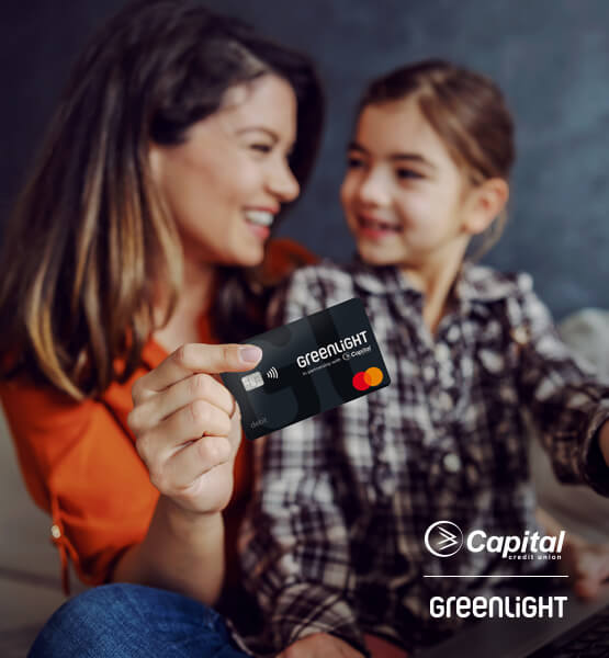 Mom with kid, holding Greenlight debit card smiling. 