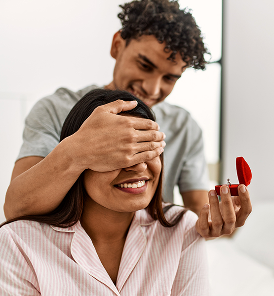 Young man covers girlfriend's eyes as he gets ready to present her with a surprise gift of jewelry