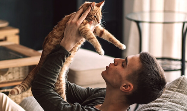 Young man holding cat up in the air inside new home.