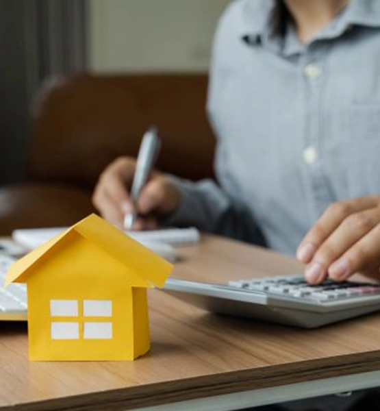 paper home on desk with person using calculator and writing in the back.