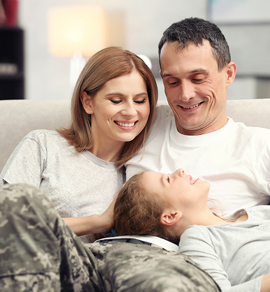 Family smiles and laughs together on living room couch at home with military veteran father