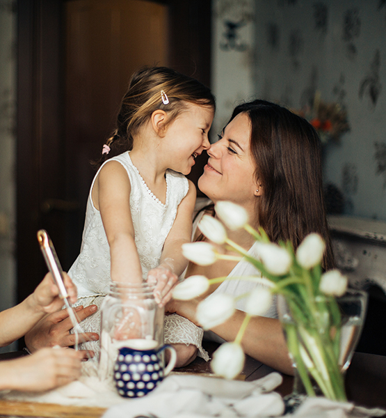 Middle aged mother rubbing noses with giggling daughter at the kitchen table at home