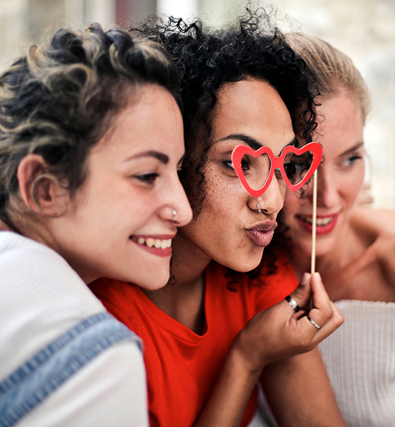 Three young women posing for a group photo with a valentines day themed prop
