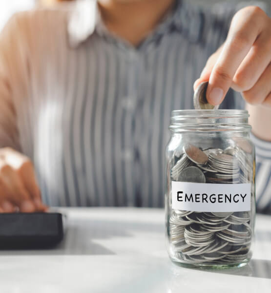 Person putting coin into emergency savings coin jar, with a calculator in the background.