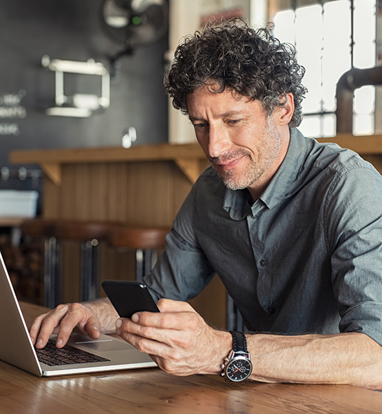 Middle aged bar owner looks up information on his laptop and dials a phone number on his cellphone