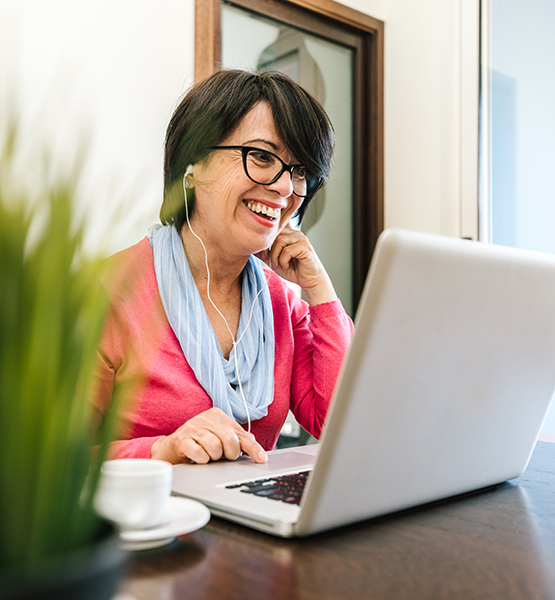 Woman approaching retirement age smiles on a video call over laptop while at home