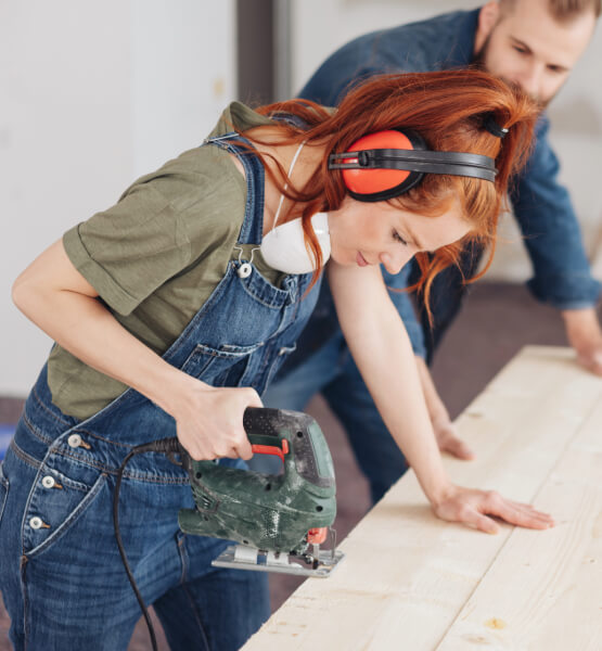 couple using power tool to cut a piece of wood inside home.